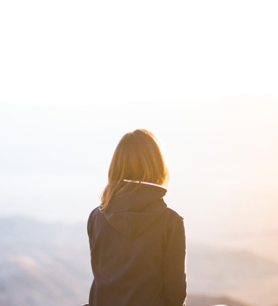 Girl with back facing image, staring across mountains during sunrise