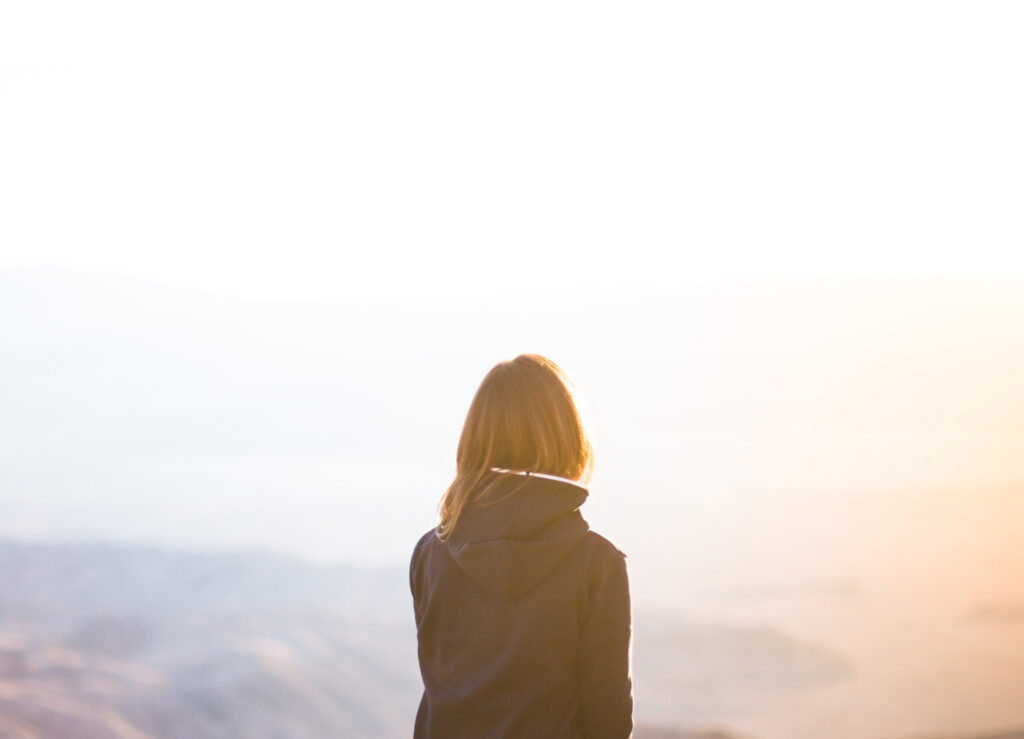 Girl with back facing image, staring across mountains during sunrise