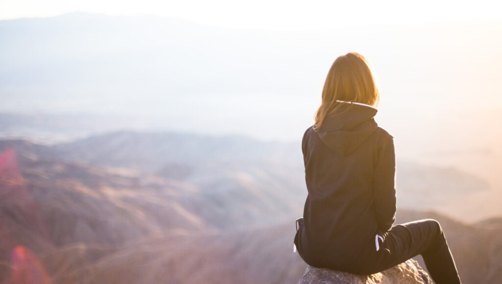 Girl with back facing image, staring across mountains during sunrise