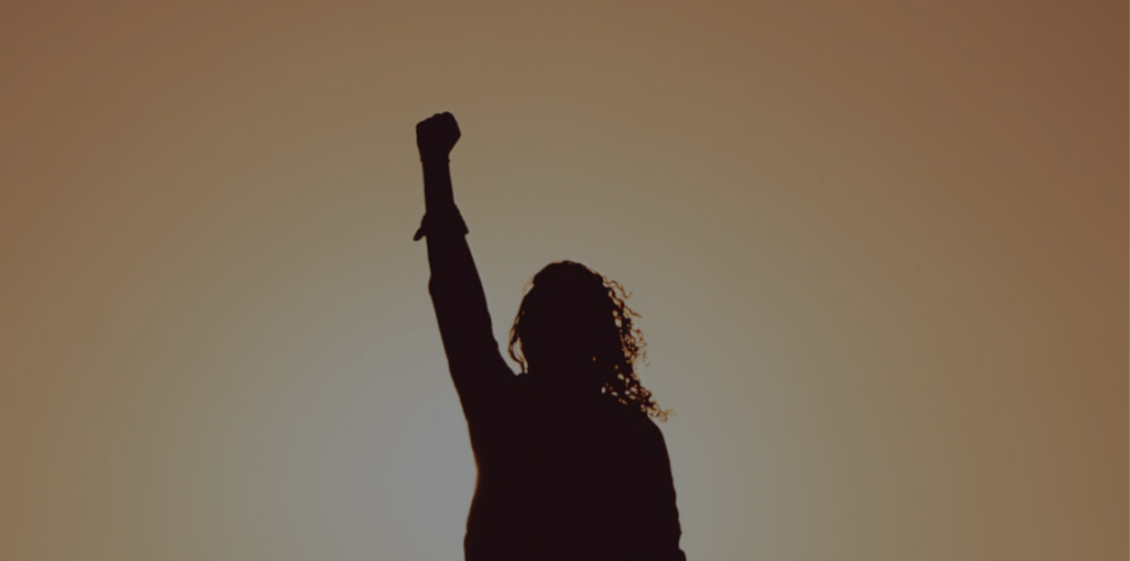 Silhouette of woman with fist in the air and sun behind her back